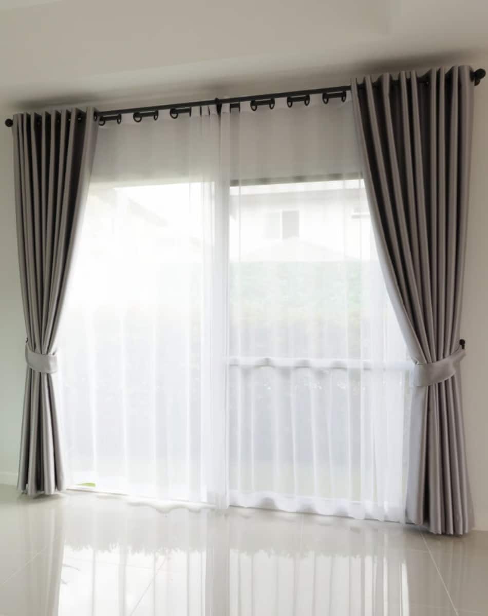 Textile curtain cleaning. Floor-length white sheer curtains layered with gray drapes in a bright room.