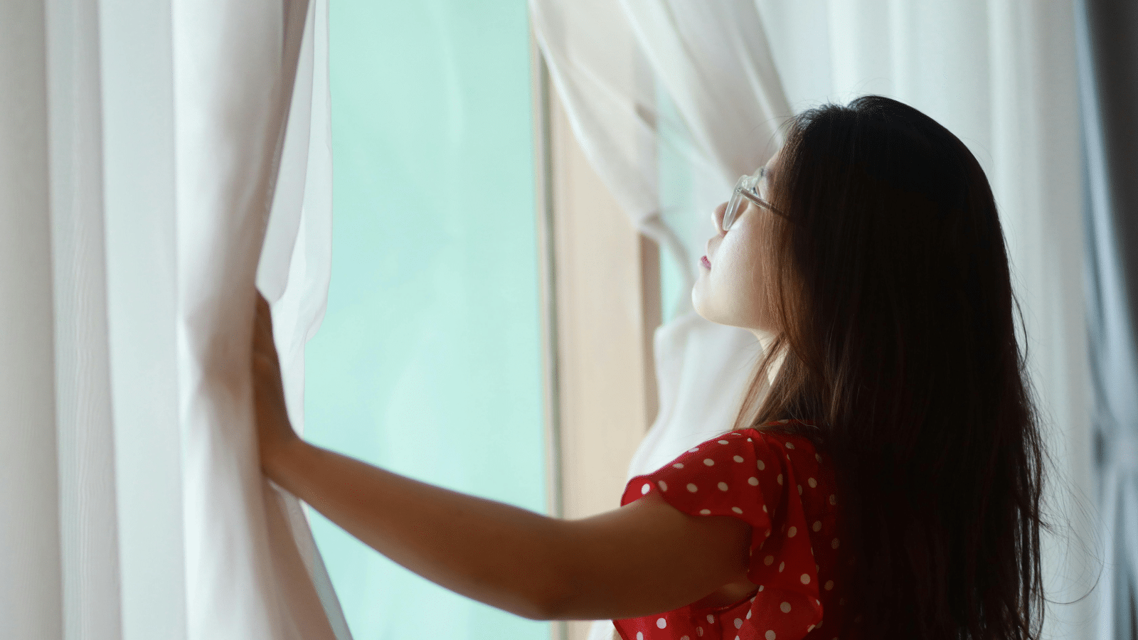 A woman looking at her window, wondering when to replace her curtains